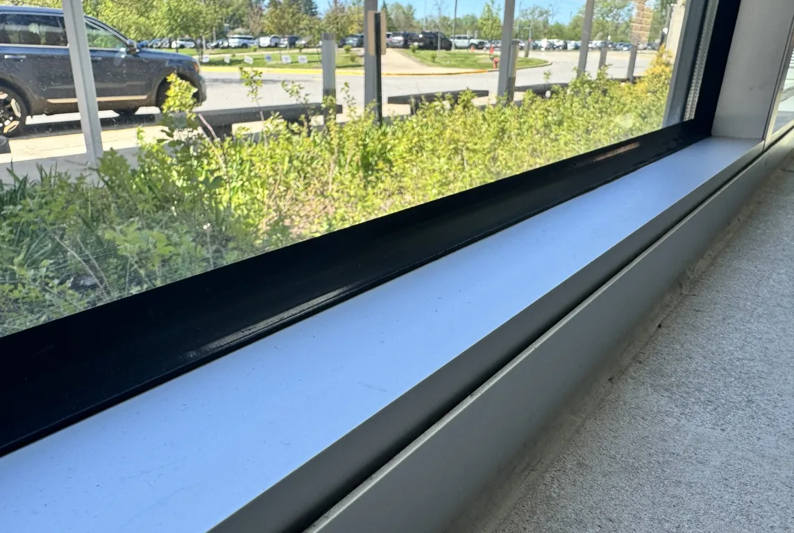 Close-up of the bottom edge of a window and its metal frame, seen from inside a school building.